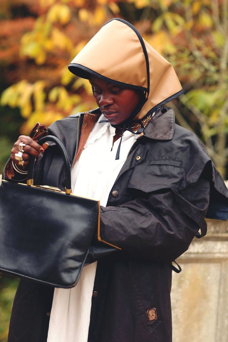 Person wearing a dark coat with a hood, holding a black handbag outdoors.