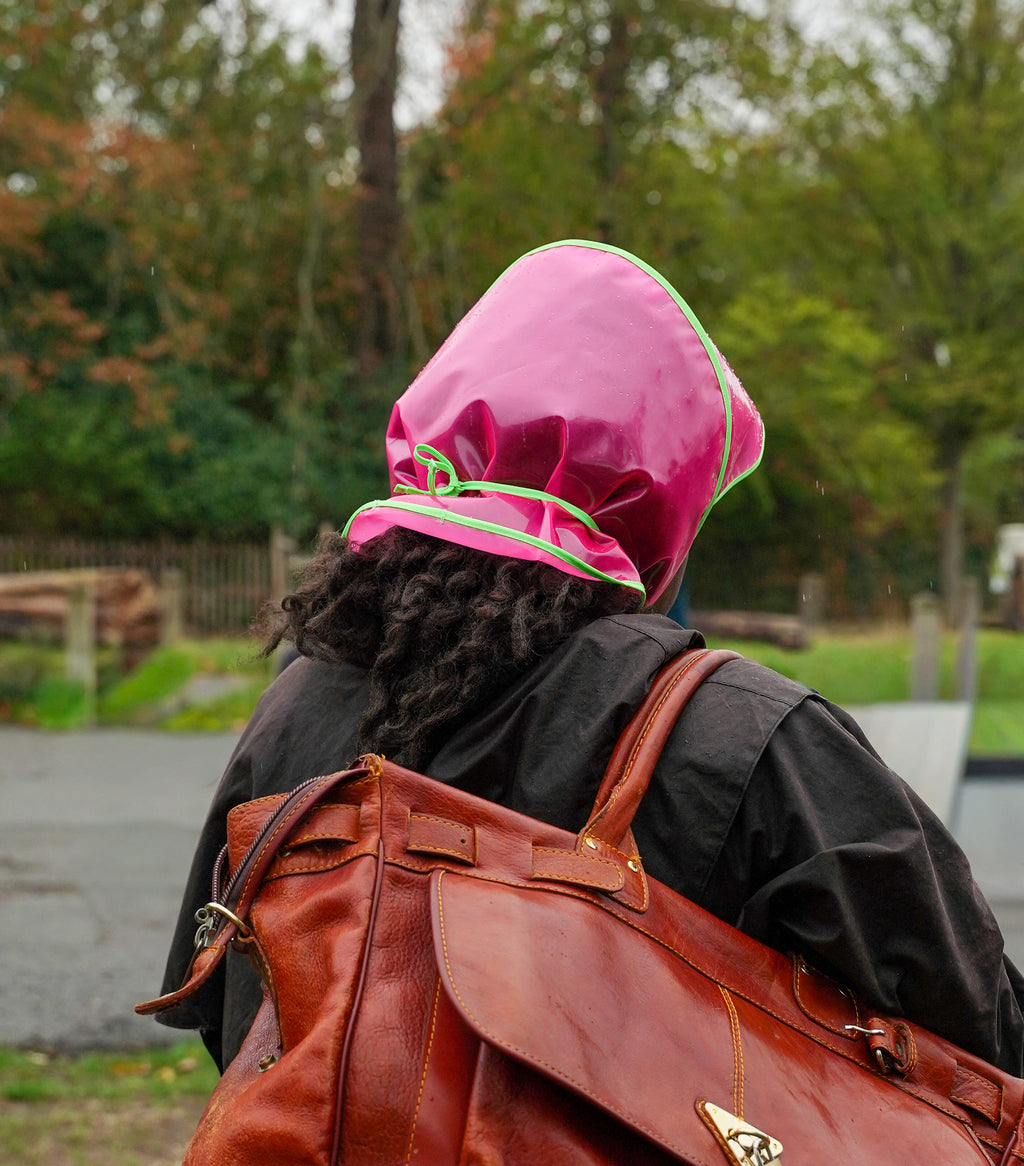 Woman cycling in a bright pink Grandmamma Jellies rain bonnet with an orange backpack