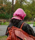 Woman cycling in a bright pink Grandmamma Jellies rain bonnet with an orange backpack